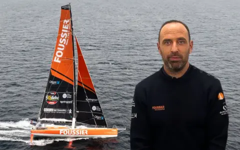 Sébastien Marsset, skipper du voilier Foussier, prêt pour la course. Le bateau orange et noir fend les vagues.