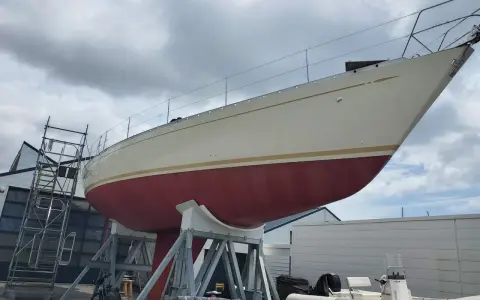 Le nouveau bateau de Jean Le Cam, un voilier blanc et rouge, est sur des supports à côté d'un atelier.