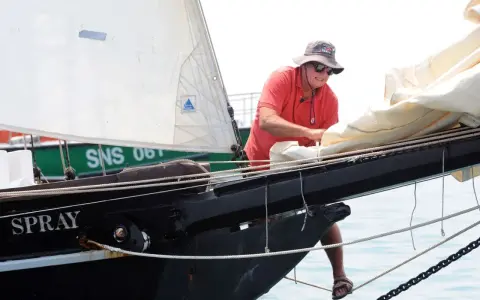 Un homme, Guy Bernardin, ajuste les voiles du Spray, un voilier historique, par une journée ensoleillée.