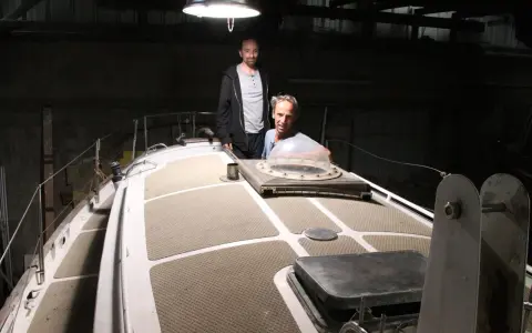 Nicole Van de Kerckhove et un autre homme sur le pont d'un voilier dans un hangar sombre.