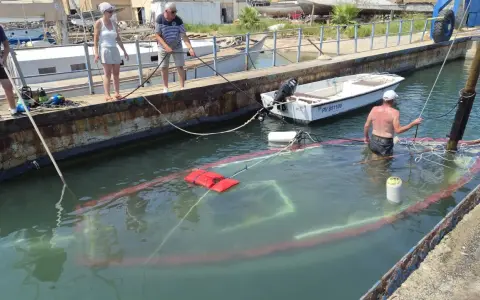 Un bateau accidenté est partiellement submergé dans un port. Des personnes sur le quai tentent de gérer la situation.