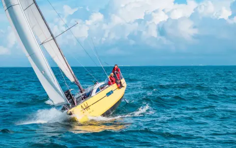 Un voilier jaune fend les vagues bleues, ses voiles blanches gonflées par le vent. L'équipage profite de cette belle journée pour faire la voile.