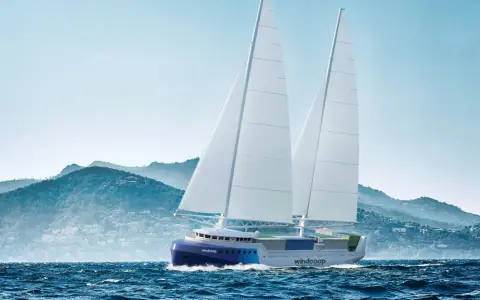 Un porte-conteneurs à voile futuriste navigue sur une mer agitée, avec des montagnes verdoyantes en arrière-plan.