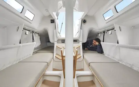 L'intérieur du voilier, premier 27, offre des couchettes confortables et un espace de vie lumineux. Un homme se repose, profitant du calme.