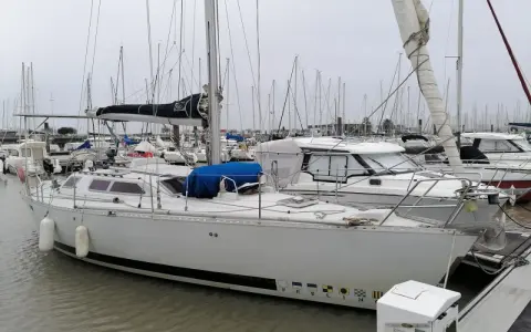 Un voilier blanc, "PEELIN", est amarré dans un chantier naval. D'autres bateaux sont visibles en arrière-plan.