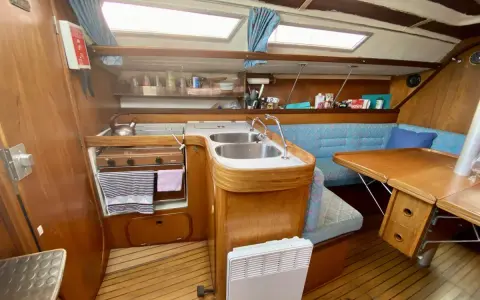 Cuisine de voilier avec cuisinière, évier double, banquette bleue et table en bois. Un radiateur est visible. 312 avis gib sea.