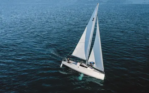 Un voilier blanc navigue sur une mer bleue. Sa quille est visible sous l'eau, stabilisant le bateau.