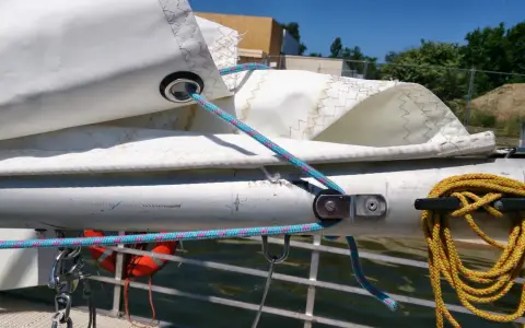 Le cordage bleu passe dans un œillet de la voile, prêt à ajuster la bosse de ris. Une amarre jaune est enroulée sur un taquet.