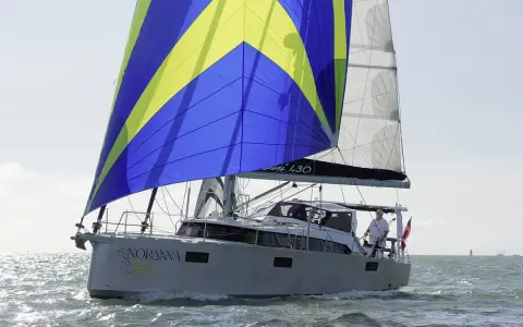Le voilier "Noranna" L430 navigue sur une mer agitée, sa grand-voile aux couleurs vives bleu et jaune captant le vent.