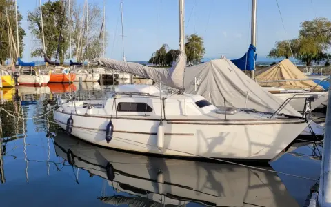 Un voilier blanc, prêt pour l'aventure, est amarré dans un port paisible. Le reflet du voilier sauvignon sur l'eau calme est saisissant.
