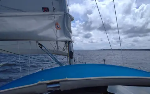 Vue depuis un voilier, avec la liste des voiles d'un bateau gonflées par le vent. La mer est agitée sous un ciel nuageux.