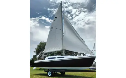 Voilier Mac Gregor 25, prêt à naviguer, avec ses voiles blanches gonflées par le vent sous un ciel nuageux.