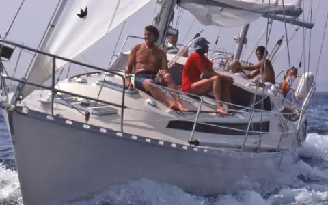 Un groupe profite d'une journée en mer sur ce qui semble être le meilleur voilier fifty, naviguant sur des eaux bleues avec des voiles blanches gonflées par le vent.