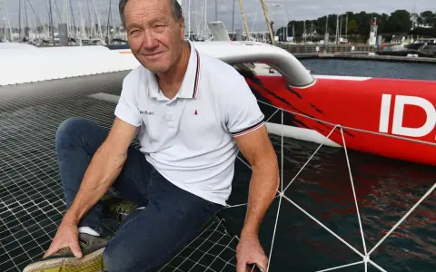 Francis Joyon, marin légendaire, pose sur le filet d'un trimaran rouge vif, prêt pour une nouvelle aventure en mer.