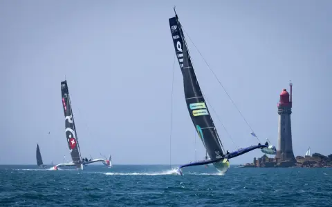 Le trimaran Koesio fend les vagues, une course intense près d'un phare.