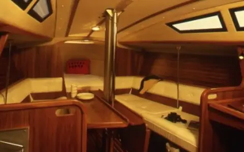 Intérieur chaleureux d'un voilier, avec banquettes en cuir crème, boiseries sombres et hublots. Le **selection 37 interieur** offre un espace confortable pour la vie à bord.