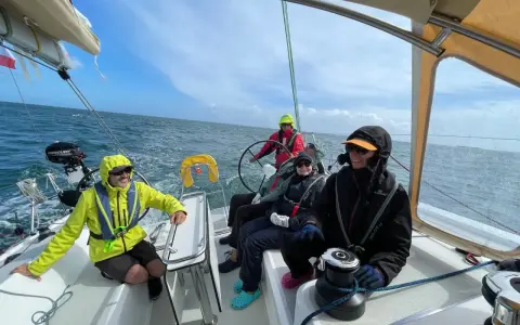 Équipage souriant sur un voilier, profitant de la navigation. Personne n'a besoin d'écoper, la mer est calme.