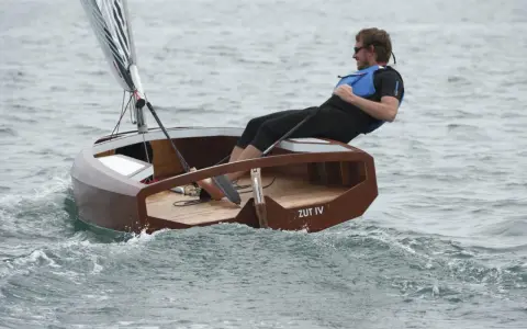 Un homme navigue sur un petit bateau en bois, le "ZUT IV", dans une mer agitée.
