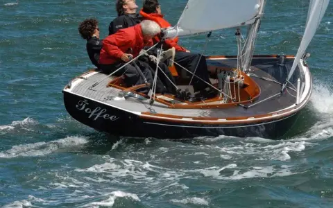 Le voilier "Toffee" navigue sur une mer agitée, quatre personnes à bord profitent de la balade.
