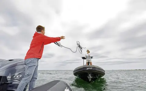 Un jeune homme lance une corde pour le remorquage d'un bateau en panne. Une femme attend sur l'autre embarcation.