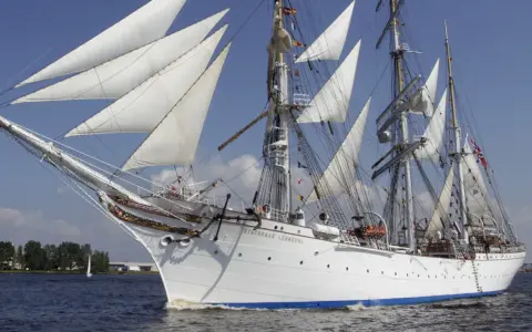 Le Statsraad Lehmkuhl, voilier blanc aux voiles gonflées, navigue fièrement, symbole du **general valor** des marins.