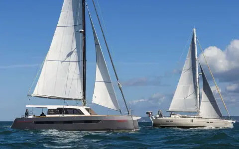 Deux voiliers naviguent sur une mer bleue. L'un est un catamaran gris moderne, l'autre un voilier blanc classique. Une belle journée pour déguster un voilier fruit de mer.