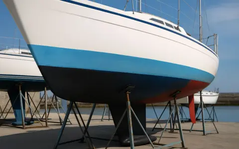 Vue rapprochée de la coque d'un voilier blanc avec une bande bleue et une bande rouge. Le choix couleur coque bateau est important pour l'esthétique.