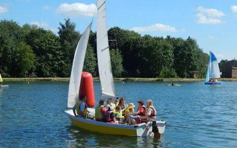 Un groupe de personnes, dont des enfants, profite d'une journée ensoleillée sur un bouchain bateau jaune. Un autre bateau à voile bleu navigue au loin.