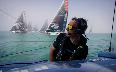 Franck Cammas, concentré, navigue en tête d'une flotte de voiliers dans le brouillard.