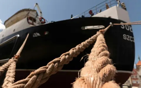Gros plan sur des cordages épais assurant l'amarrage d'un bateau noir et blanc, avec des bâtiments colorés en arrière-plan.