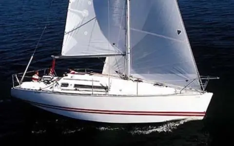 Voilier blanc à voiles gonflées, naviguant sur l'eau sombre. Les avis sur le Sun Fast 32 confirment sa rapidité.