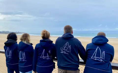 Cinq personnes portent des vestes bleues avec des voiliers dessinés. Benoit Marie et ses amis admirent la mer.