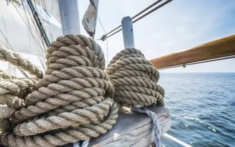 Gros cordages enroulés sur des taquets, prêts pour l'aventure. La proue du bateau fend les flots bleus sous un ciel clair.