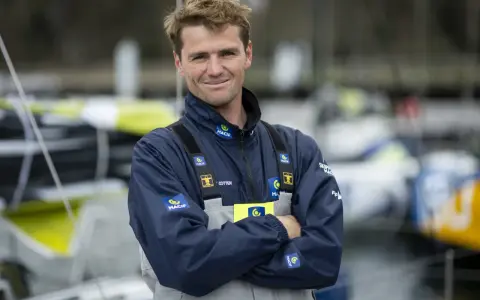 L'athlète marin Lois Berrehar, souriant, porte une veste bleue MACIF avec des logos. Derrière lui, des voiliers colorés.