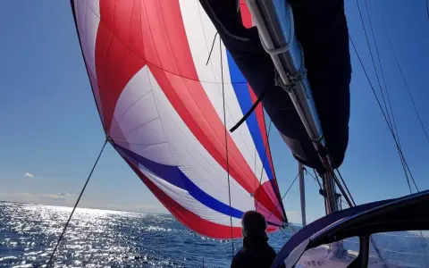 Un spi symétrique aux couleurs vives gonflé par le vent, naviguant sur une mer scintillante sous un ciel bleu clair.
