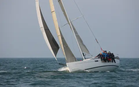 Équipage sur un voilier blanc, le foc et le génois gonflés par le vent, naviguant sur une mer agitée.