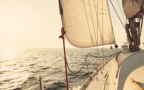 Voile de bateau gonflée par le vent, naviguant sur une mer calme au coucher du soleil.