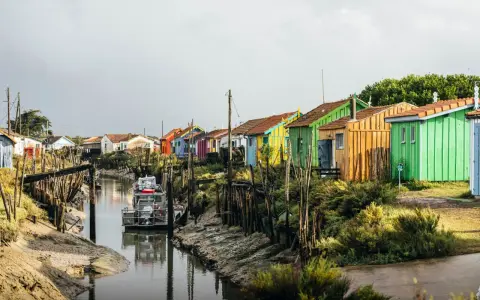 Cabanes colorées alignées le long d'un canal, un bateau amarré. Un charmant port sur l'Île d'Oléron.