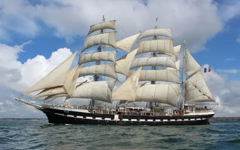 Le Belem, majestueux trois-mâts, navigue fièrement sous un ciel bleu et nuageux, rappelant les grandes traversées vers Bayonne.