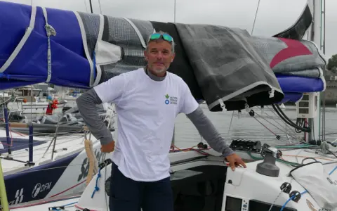 Gildas Mahé, skipper, pose sur son voilier, prêt pour une nouvelle aventure maritime.