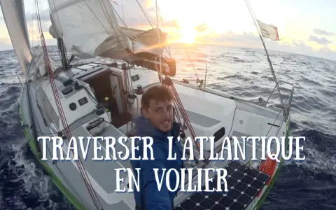 Un homme souriant sur un voilier en pleine traversée de l'Atlantique. Le soleil se lève, illuminant les voiles. Quel voilier pour traverser l'Atlantique ? Celui-ci semble parfait.