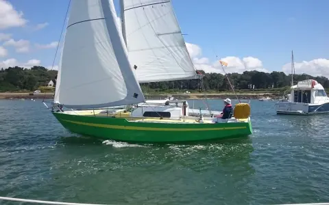 Un voilier vert vif navigue sur l'eau, avec un autre bateau à moteur en arrière-plan. Une belle journée pour une croisière, peut-être avec une dégustation d'armagnac à bord de ce bateau.