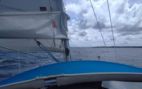 Vue depuis un voilier, le **lofer voile** blanc gonflé par le vent, sur une mer agitée sous un ciel nuageux.