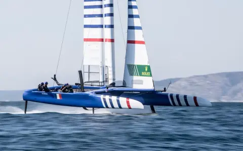 Catamaran bleu et blanc, voiles rayées, en pleine action. La **vitesse catamaran** est impressionnante, les foils hors de l'eau.