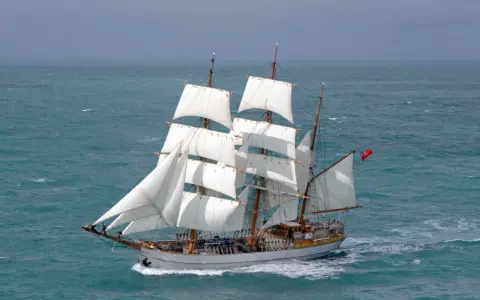 Majestueux voilier 3 mats, ses voiles blanches gonflées par le vent, navigue sur une mer agitée.
