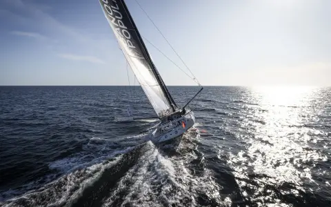 Voilier Banque Populaire naviguant au soleil, l'eau éclabousse le long du babord tribord.