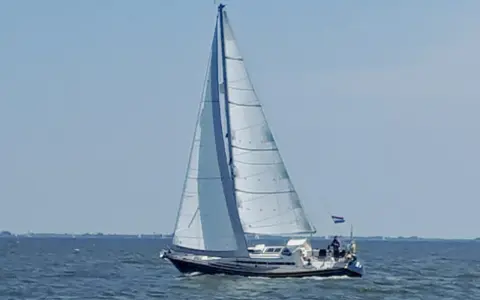 Voilier blanc et bleu naviguant sur une mer calme sous un ciel clair. Les voiles sont gonflées par le vent. Les premiers 375 avis sur ce type de bateau sont positifs.