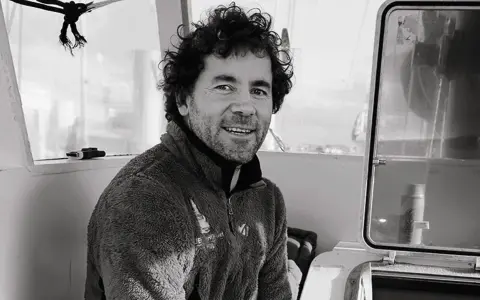 Sébastien Roubinet, un aventurier souriant, pose à l'intérieur d'un bateau, prêt pour sa prochaine expédition.