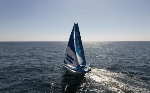 Voilier bleu et blanc "Inter Invest" naviguant sur une mer calme. Matthieu Perraut, skipper, est à la barre.
