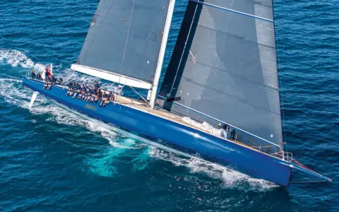 Un grand voilier bleu glisse sur l'eau, tel un tapis volant bateau. L'équipage est à bord, profitant de la navigation.